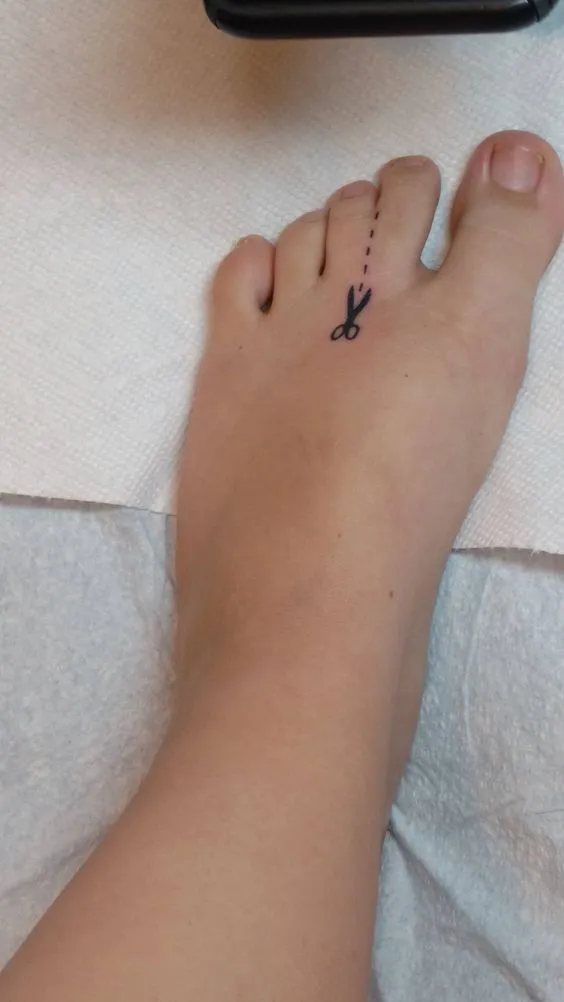 Tatuagem nos pés de tesoura com pontilhados indicando "corte aqui".
