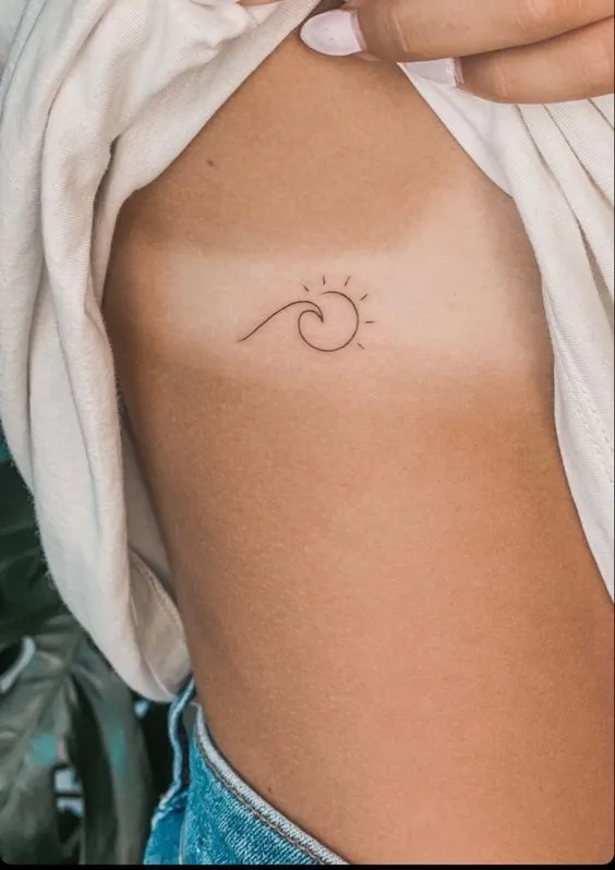 Tatuagem de traços finos onde o desenho de uma onda se funde com as formas de um sol
