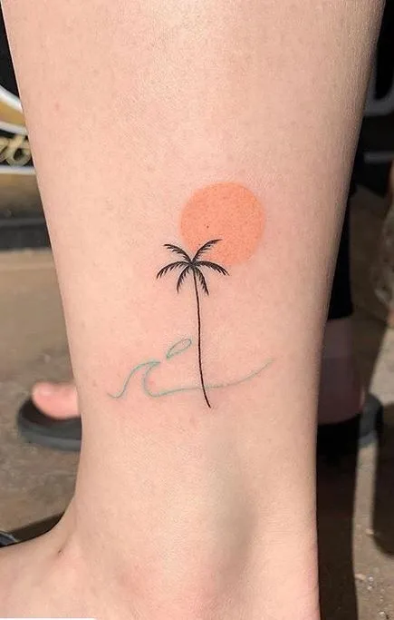 Tatuagem de um sol, uma palmeira e uma onda, em traços finos e cores pasteis