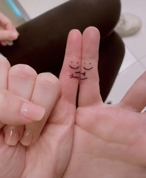 Tatuagem de casal nos dedos mindinhos com um desenho de dois bonequinhos que parece que estão se abraçando.