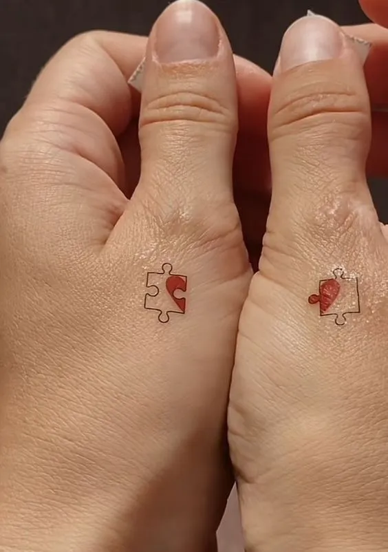 Tatuagem de casal nos dedos polegadres de um quebra-cabeça de coração.