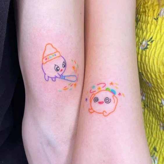 tatuagem de casal onde em um braço tem um personagem dando uma paulada e no outro braço outro personagem com estrelas na cabeça.