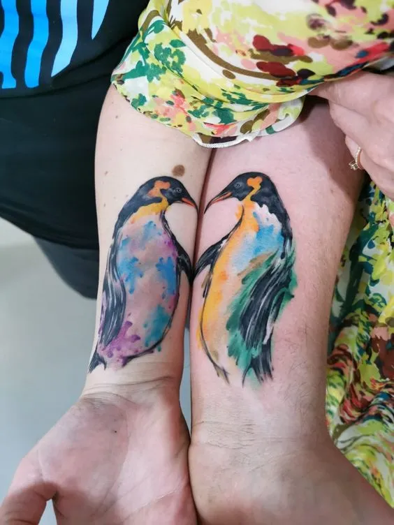 Tatuagem de casal onde cada braço tem um pinguim e quando se junam parece estarem se beijando.