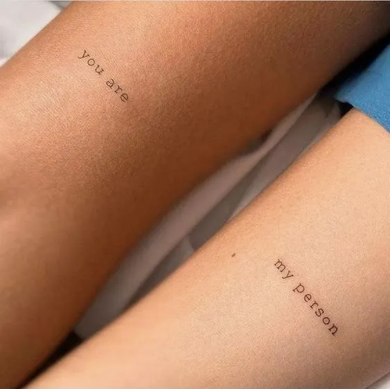 Tatuagem de casal onde um braço está escrito "You are" e no outro "My person"