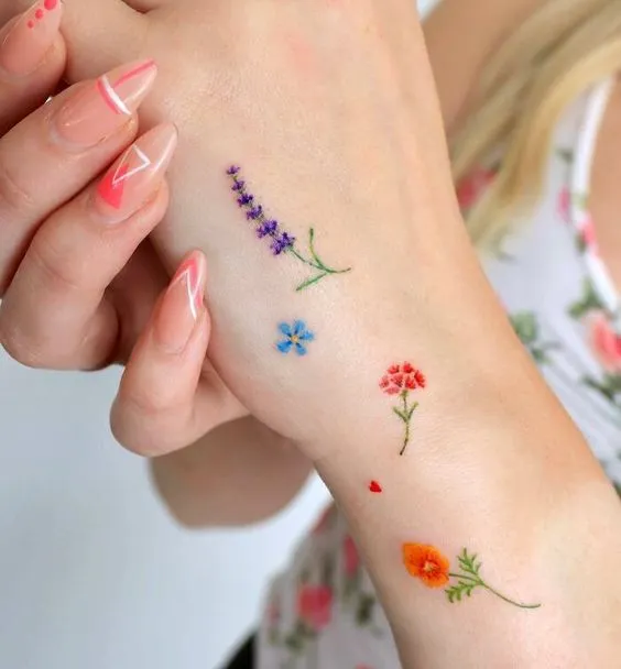 tatuagem na lateral da mão de diversas flores pequenas e coloridas