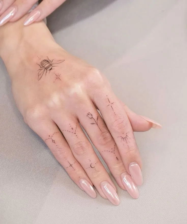 Tatuagem delicada fineline de uma abelha nas costas da mão e plantinhas nos dedos